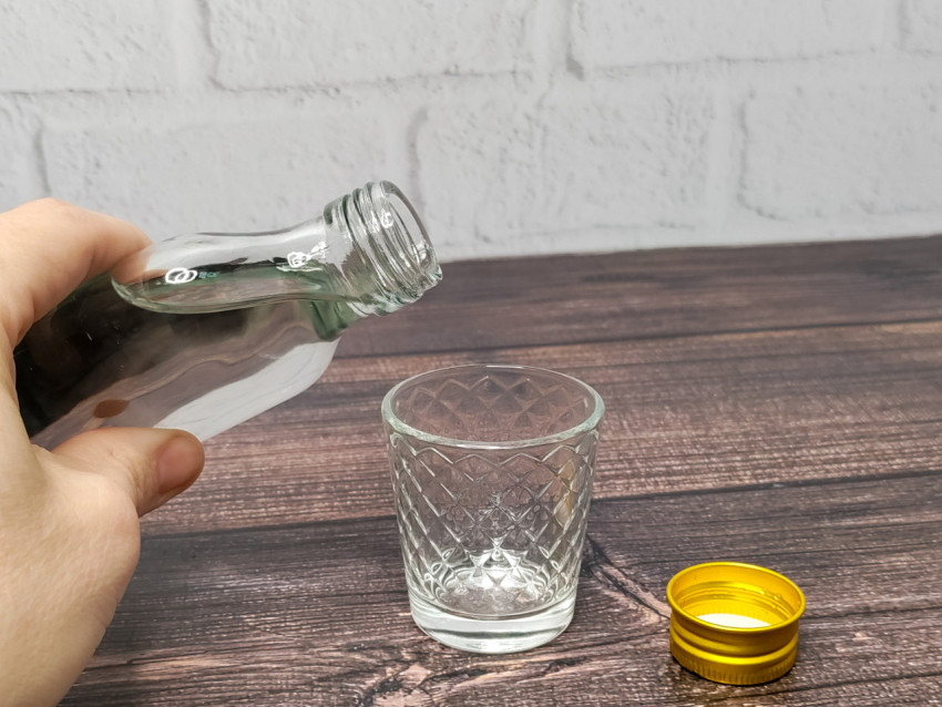 Рука наливает водку из бутылки в стопку