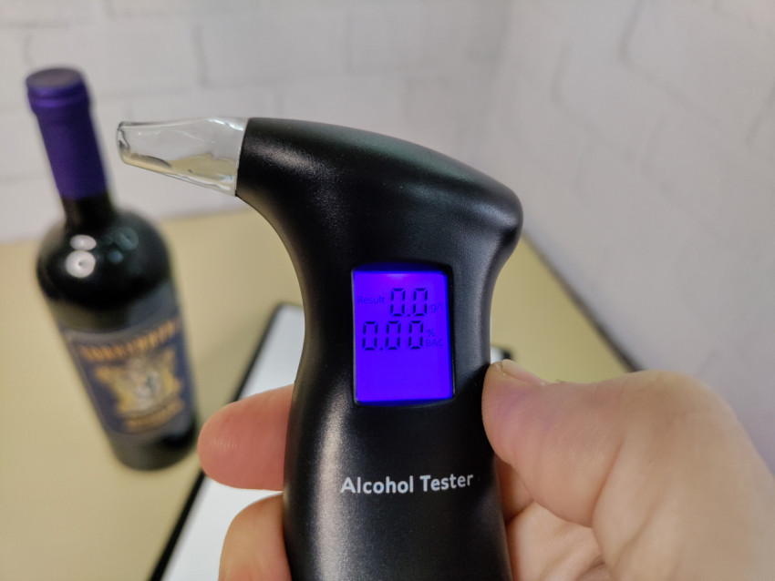 Цифровой алкотестер с нулевым показателем рядом с бутылкой вина