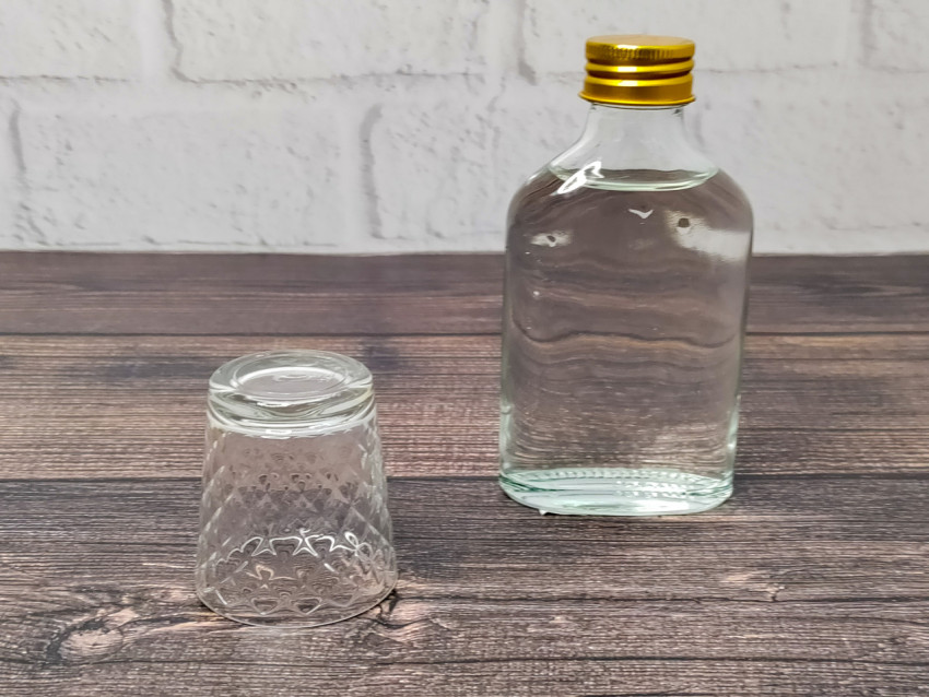 Стеклянная бутылка с водкой и перевёрнутая стопка рядом