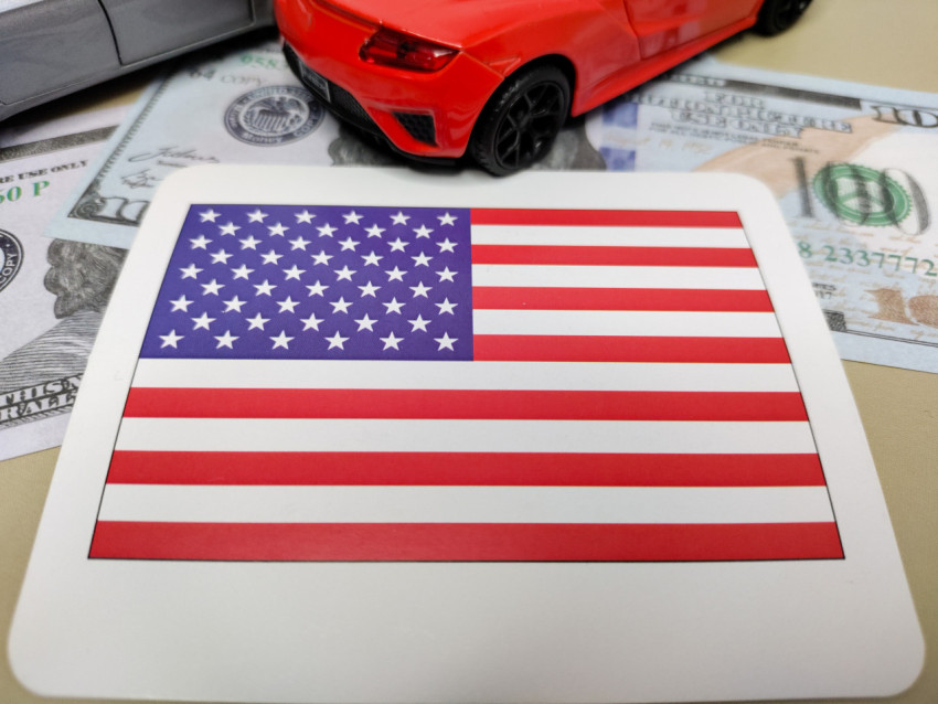 Флаг США на фоне долларов и красной модели автомобиля