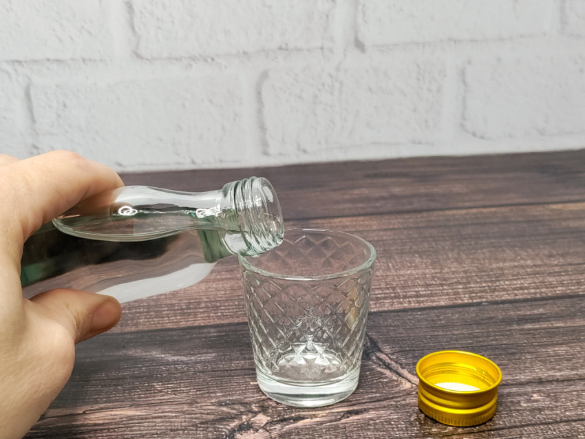 Наливание водки из бутылки в стопку на деревянном столе