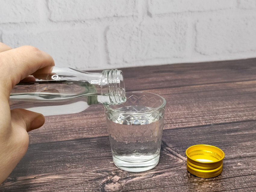 Наливание прозрачной жидкости в стакан на деревянной поверхности