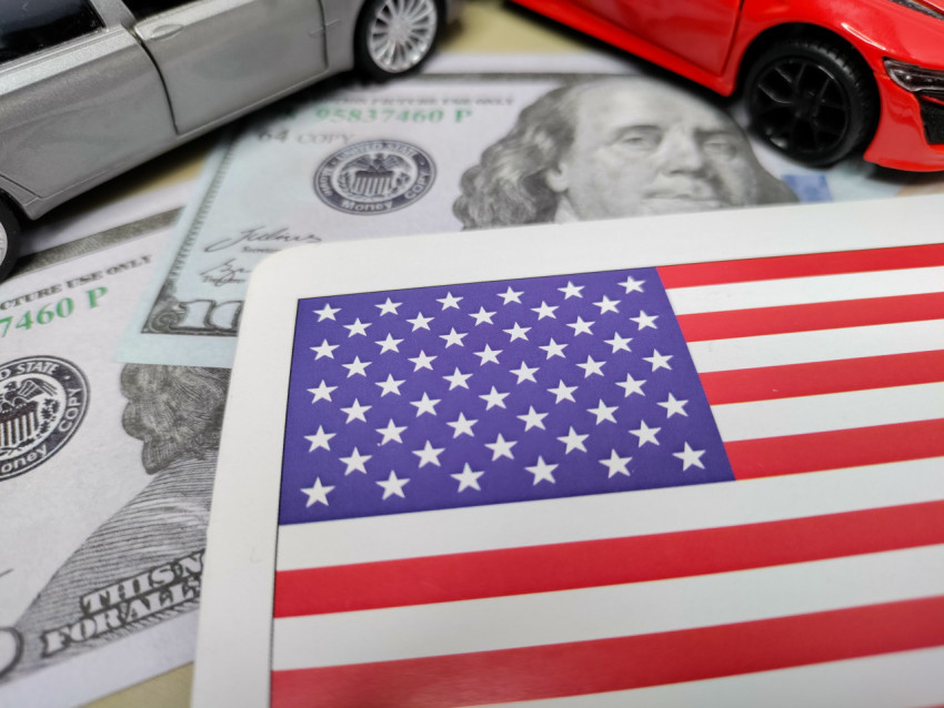 Флаг США и миниатюрные автомобили на фоне купюр с Бенджамином Франклином
