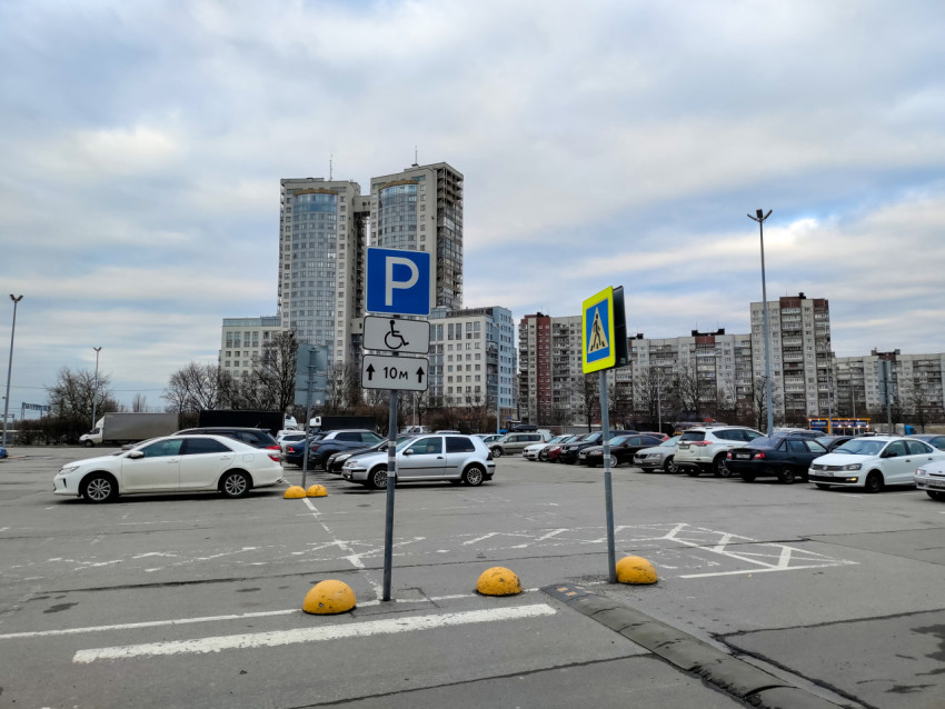 Дорожные знаки парковки и пешеходного перехода на фоне густой жилой застройки