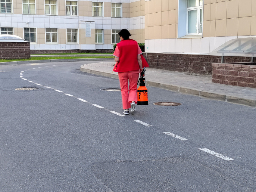 Сотрудница с оранжевым распылителем на дорожке больницы Боткина