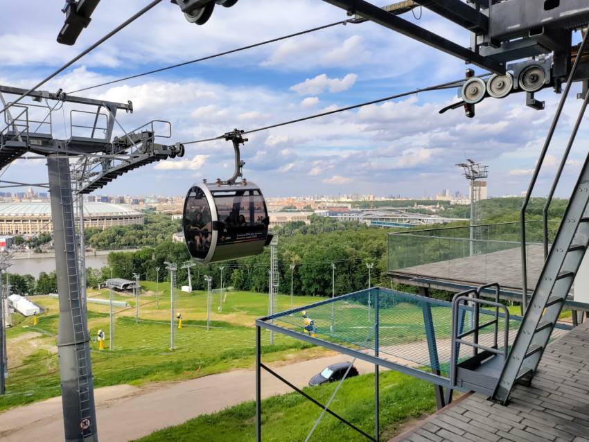 Канатная дорога над зелёным склоном с панорамой Москвы