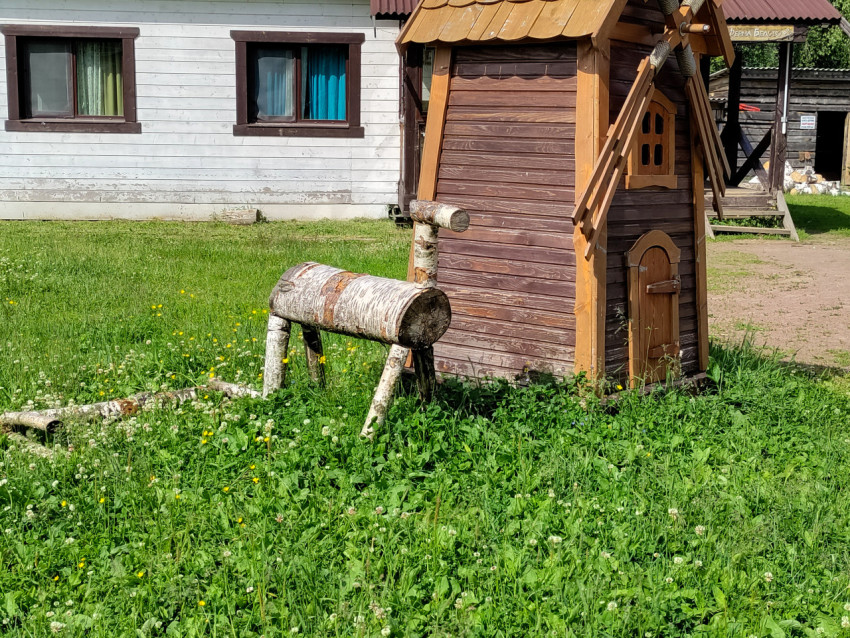 Декоративная деревянная мельница и фигурка из берёзового бревна на зелёной лужайке