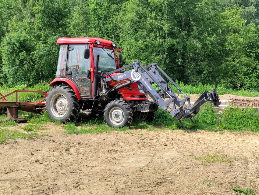 Трактор с погрузчиком TURS-400, вид сбоку на сельской площадке