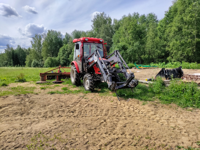 Трактор с навесным оборудованием на песчаном участке возле лесополосы