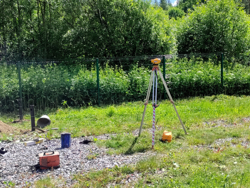 Геодезический нивелир на штативе и рейка при разметке площадки под свайный фундамент