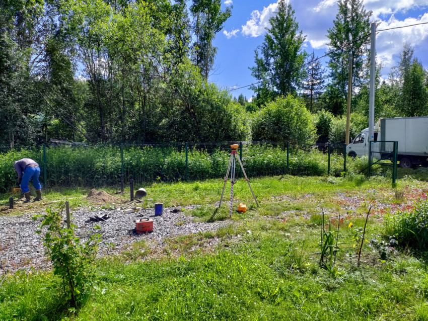 Геодезический прибор на штативе и монтаж свайного фундамента на участке рядом с фургоном