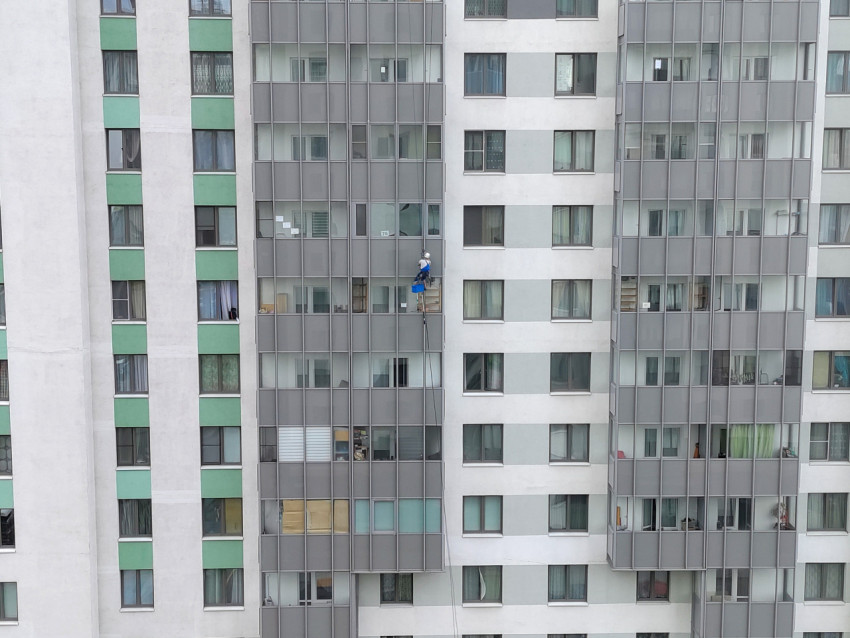 Промышленный альпинист на подвесной системе у остеклённой секции жилого дома