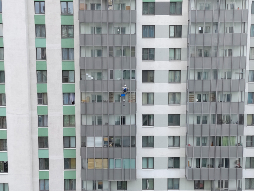 Промышленный альпинист на верёвках выполняет работы на фасаде многоэтажного жилого дома
