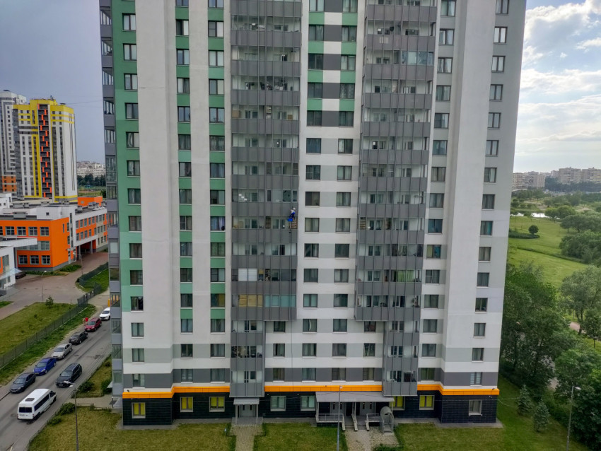 Общий вид многоэтажного жилого дома и двора, где рабочий выполняет высотные работы на фасаде