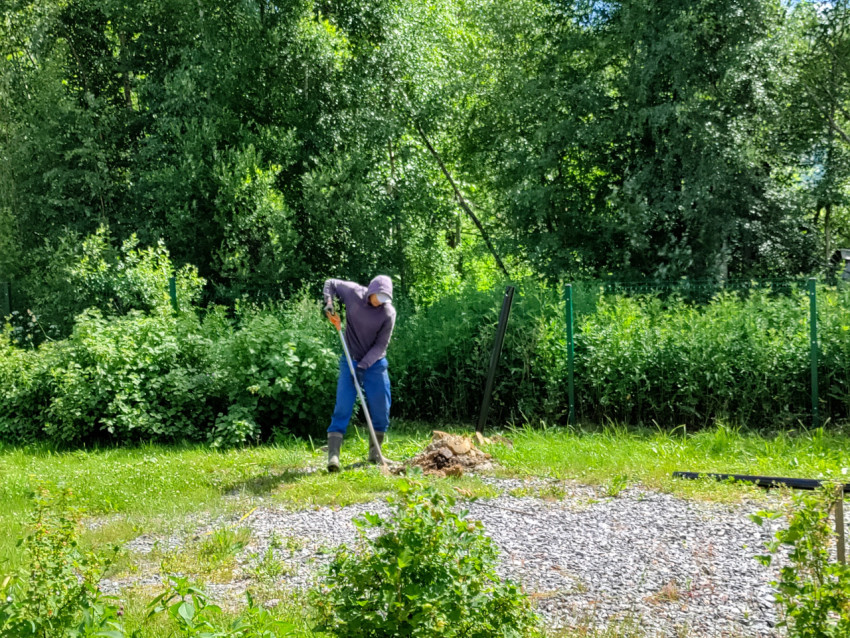 Рабочий копает лунку под сваю свайного фундамента на травяном участке у леса