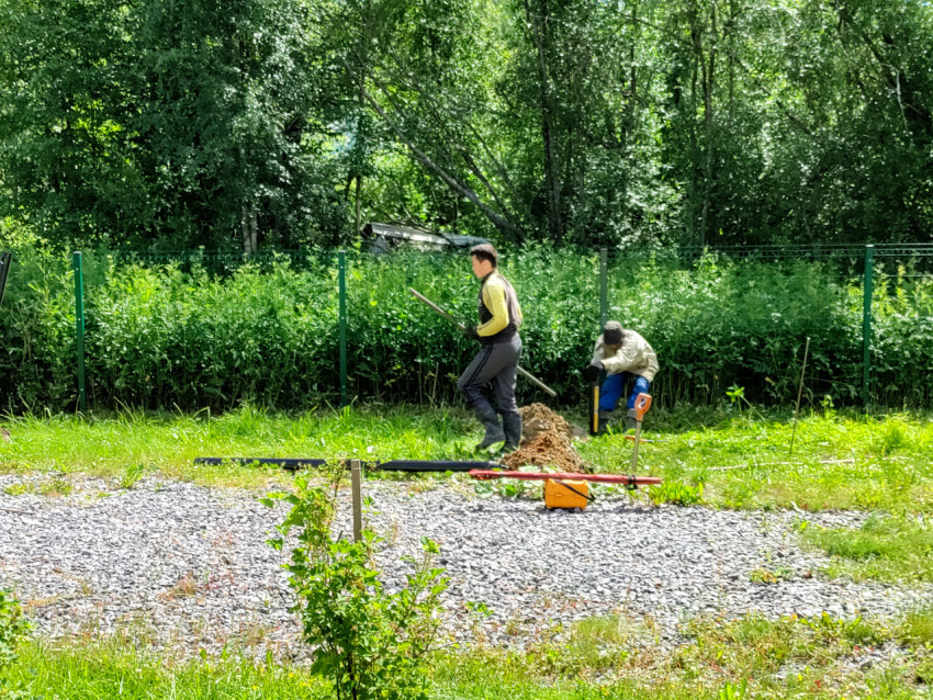 Рабочие выполняют установку свайного фундамента у ограждения на подготовленной площадке