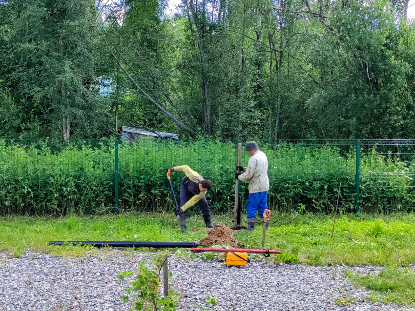Двое рабочих устанавливают сваю и готовят лунку для свайного фундамента на участке