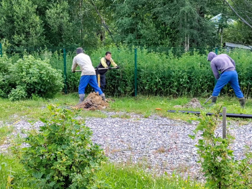 Рабочий готовит лунку, пока двое завинчивают винтовую сваю для свайного фундамента