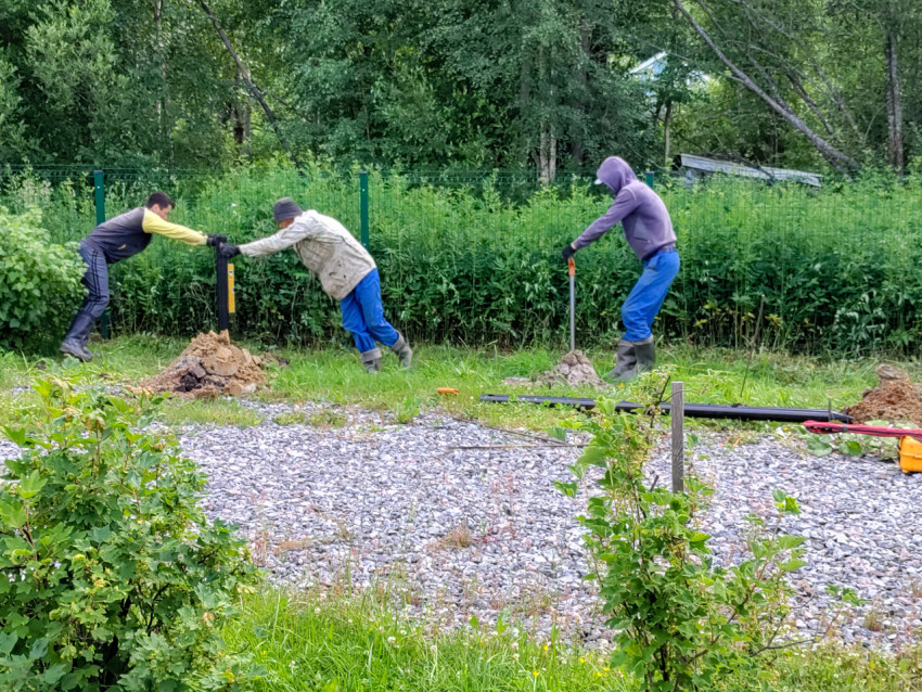 Бригада выравнивает винтовую сваю при монтаже свайного фундамента вдоль линии ограждения