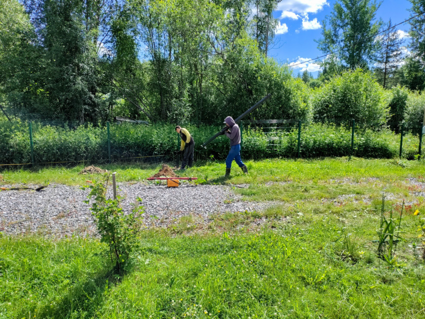 Рабочий переносит винтовую сваю для устройства свайного фундамента на участке