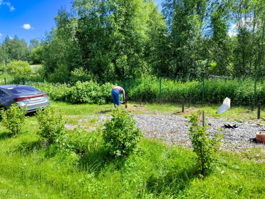 Рабочий закрепляет сваю механизированным инструментом при устройстве свайного фундамента на участке