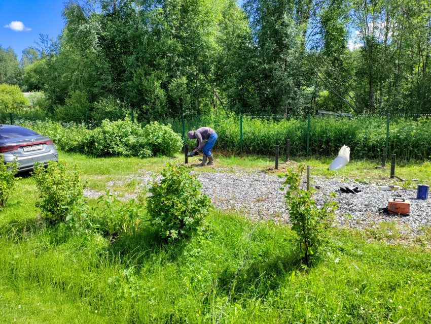 Рабочий выполняет монтаж элемента свайного фундамента на участке с щебеночной подсыпкой