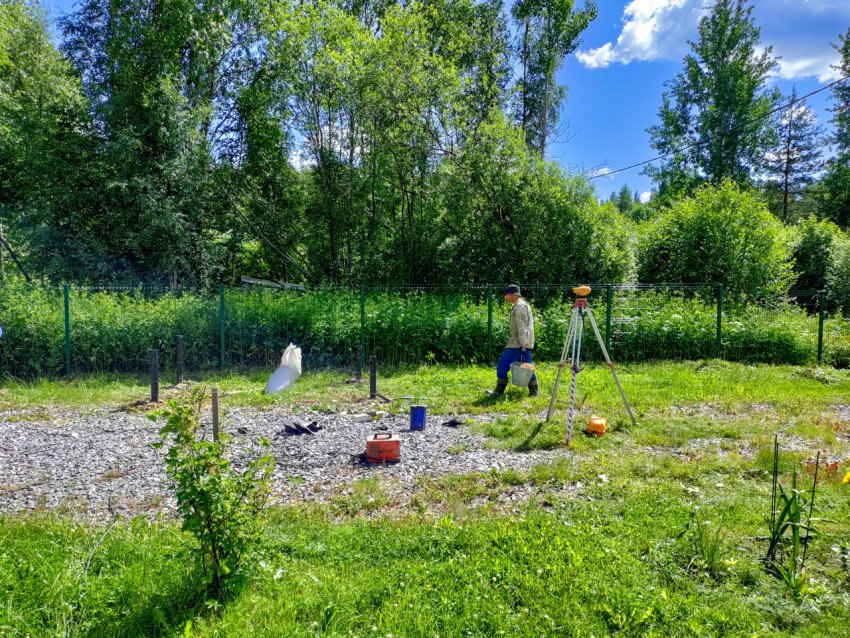 Геодезический прибор на штативе и рабочий на площадке монтажа свайного фундамента