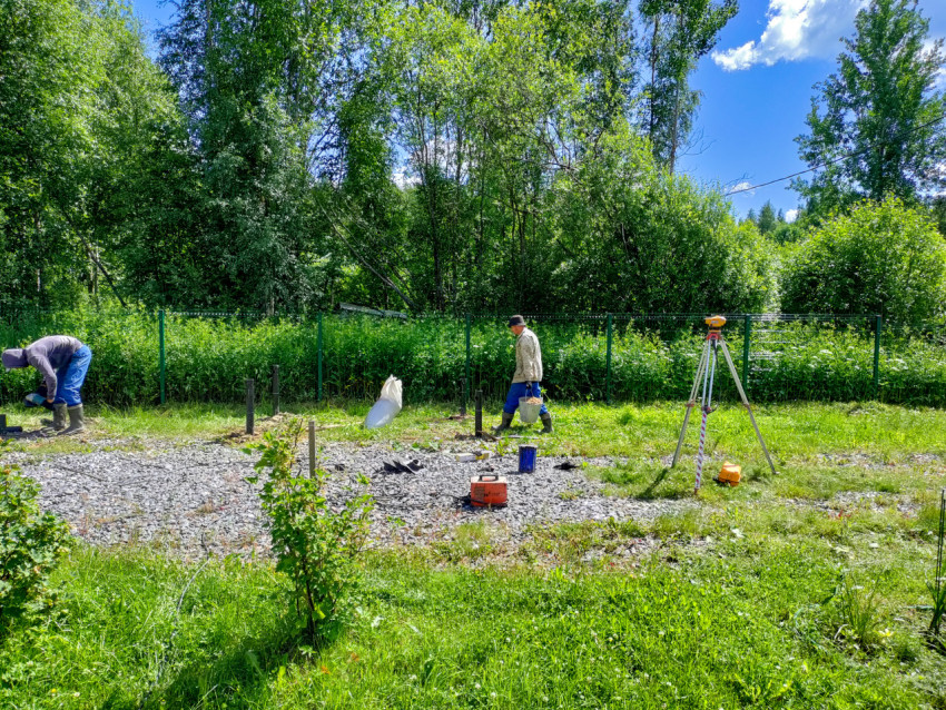 Два рабочих и геодезический штатив на площадке установки свайного фундамента