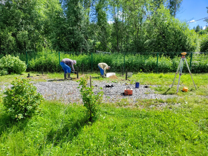 Рабочие монтируют свайный фундамент и выполняют подготовку площадки под геодезический контроль