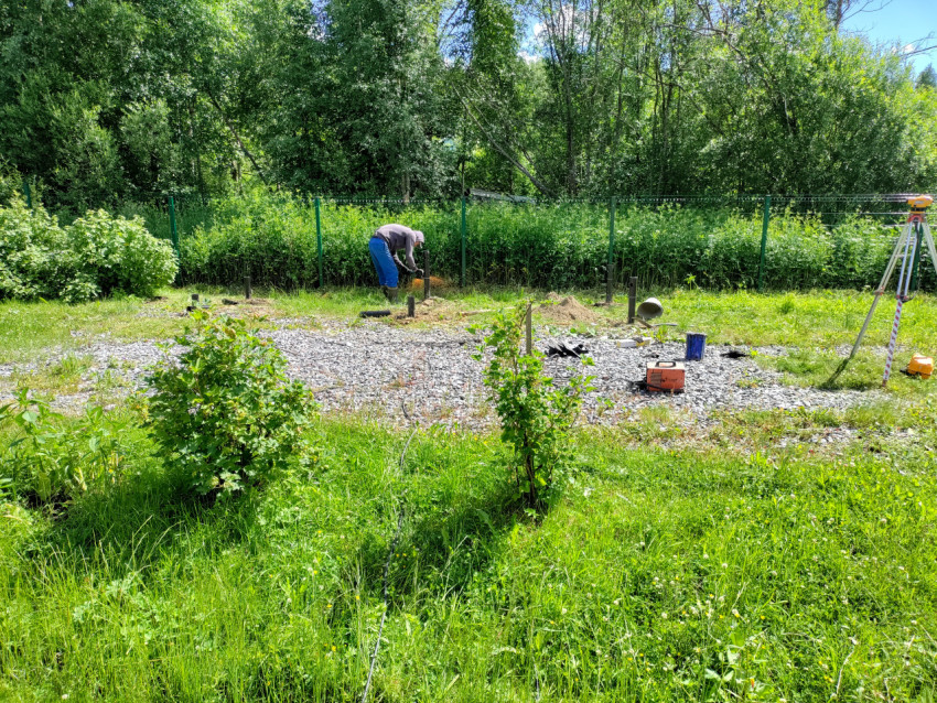 Рабочий выполняет операцию у сваи при монтаже свайного фундамента на участке