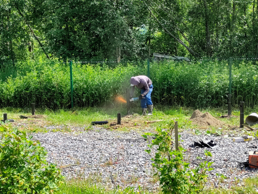Подрезка металлического столба болгаркой на щебёночной площадке при монтаже свайного фундамента