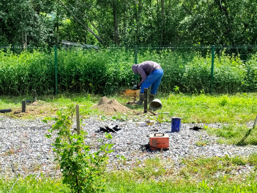 Резка металлической сваи болгаркой рядом с песком и оборудованием при устройстве фундамента