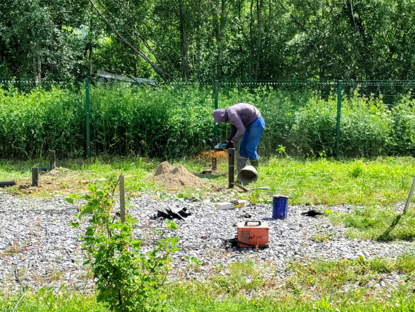 Подрезка металлической опоры болгаркой при монтаже свайного поля на участке