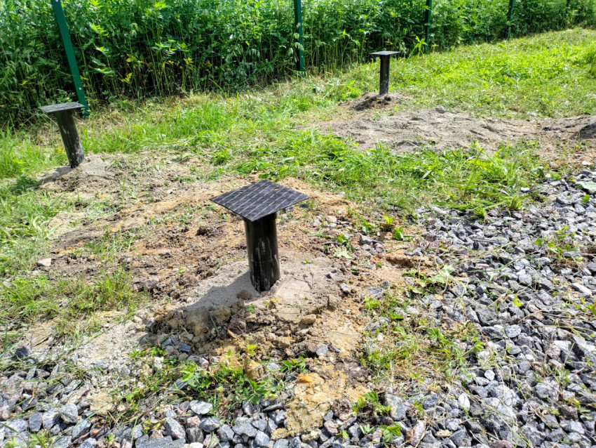 Металлические сваи фундамента с оголовками на подготовленной площадке под дом