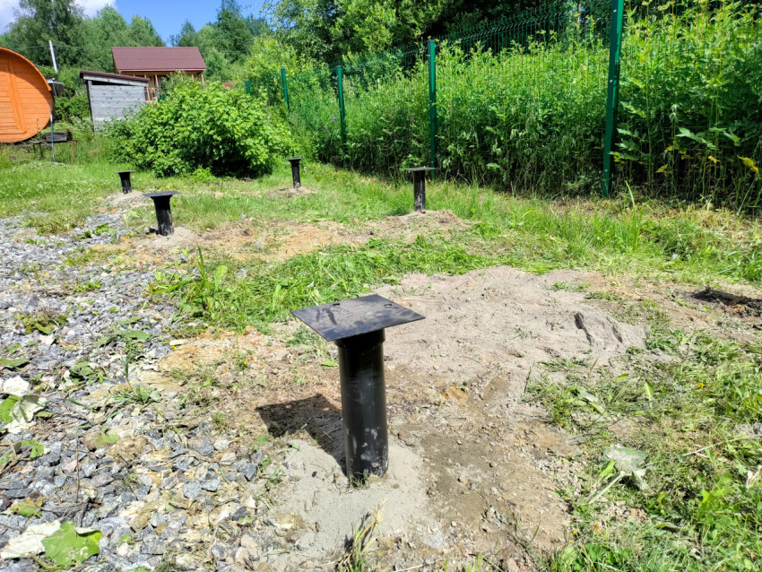 Ряд металлических свай фундамента под дом вдоль забора на загородном участке