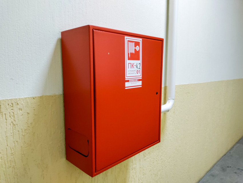 Красный пожарный шкаф на углу стены с подводящей трубой