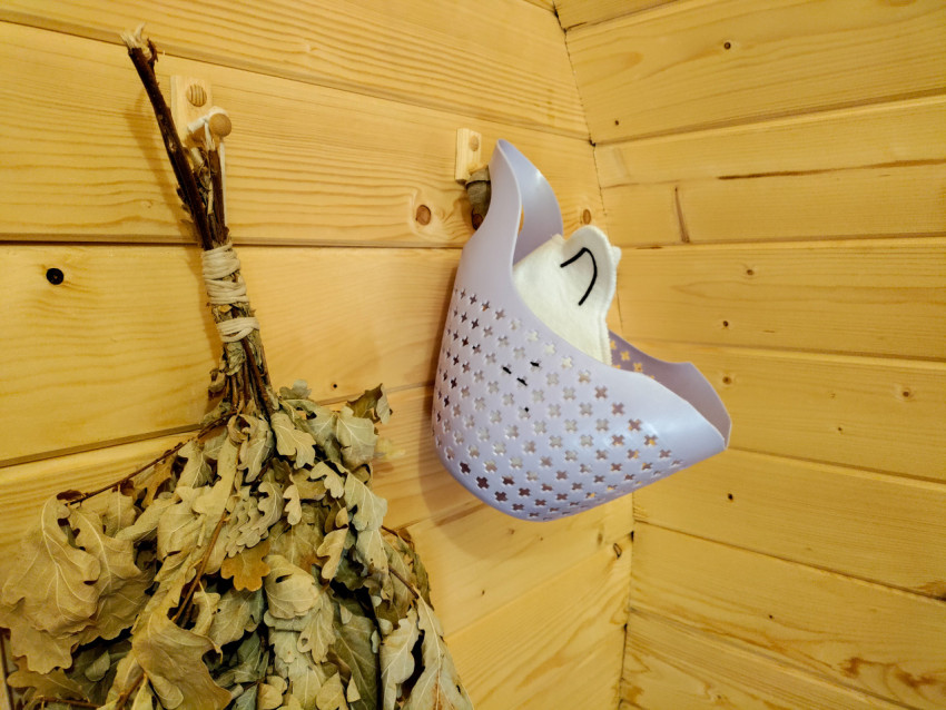 Аксессуары для бани на деревянной стене: веник, корзина и банная шапка