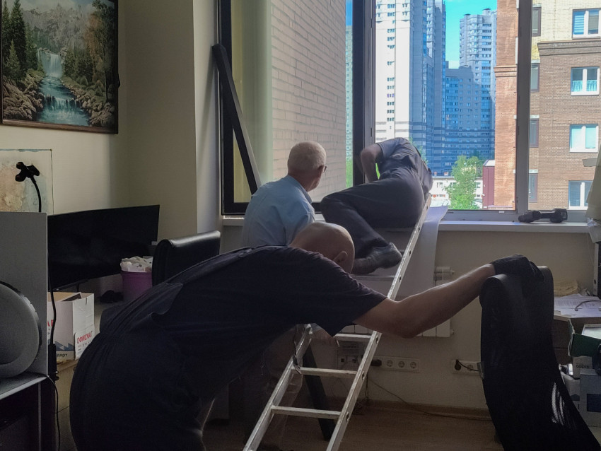 Ремонт окна в офисе с лестницей, рабочими и видом на жилые высотки за стеклом