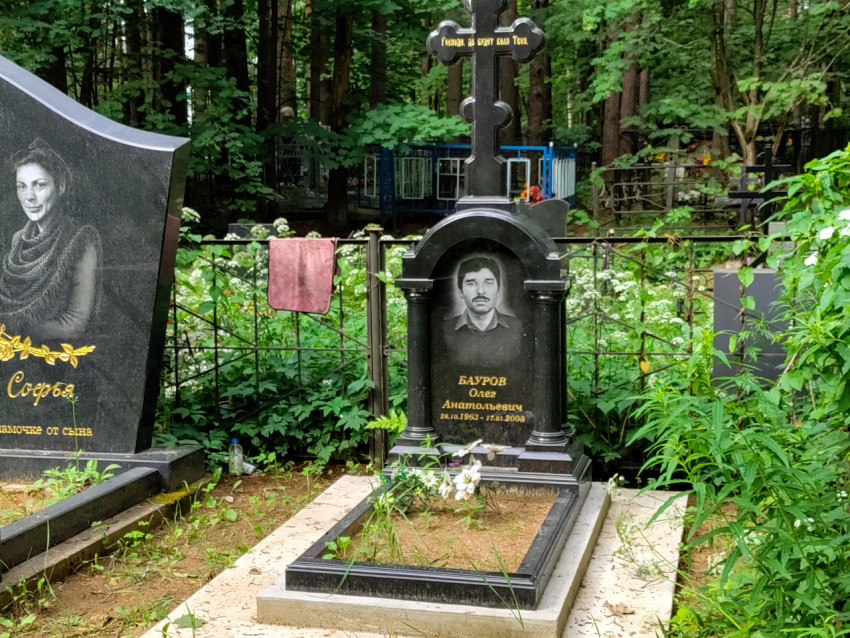 Надгробный памятник с портретом и крестом за кованой оградой кладбища