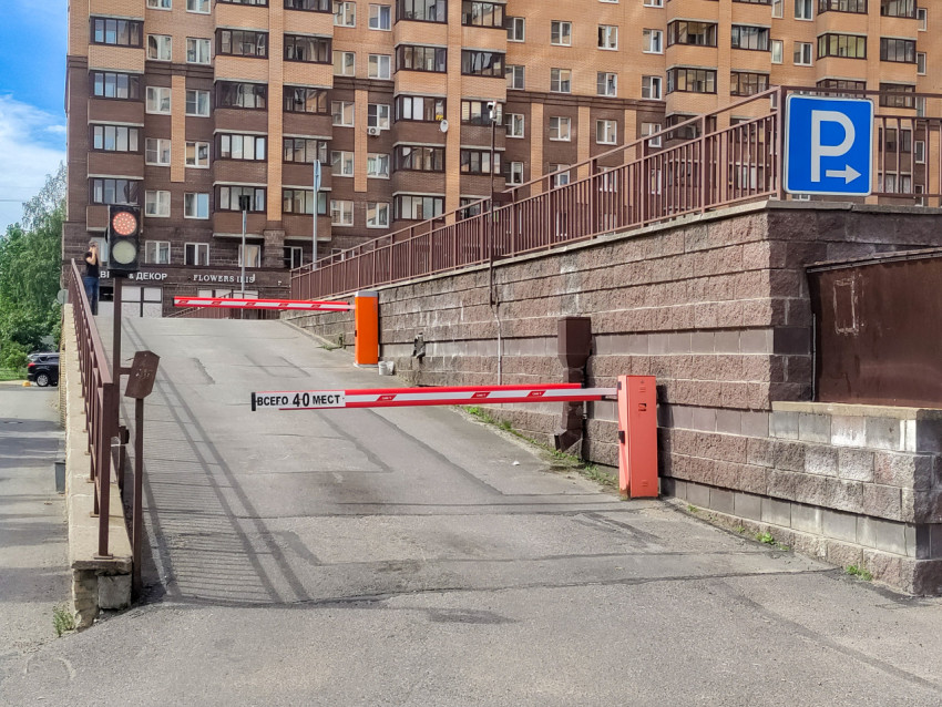 Въезд на парковку с двумя шлагбаумами, светофором и знаком «Парковка» на фоне жилого дома