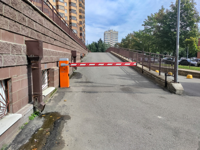 Общий вид шлагбаума на подъёмном проезде у многоэтажного дома и подпорной стены