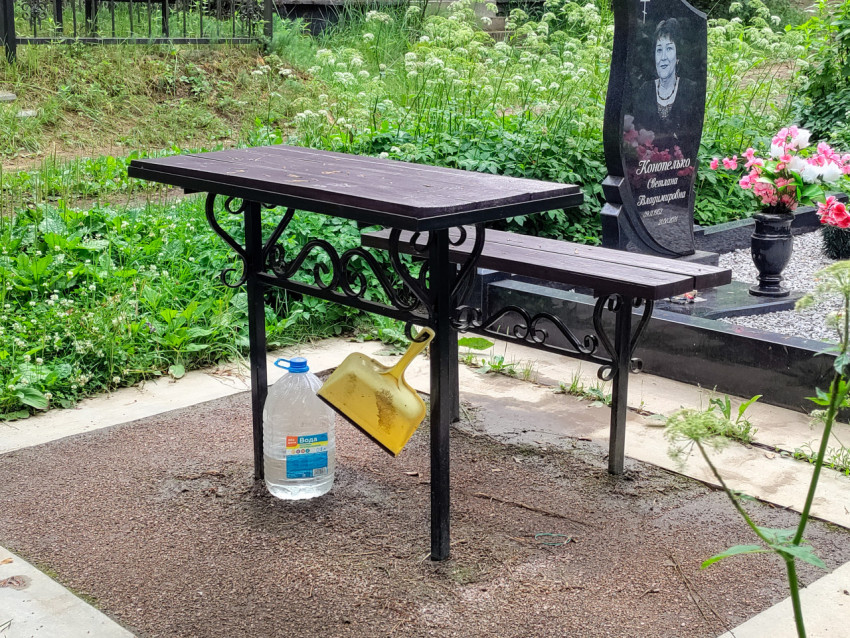 Стол и лавка для поминовения рядом с могилой и инструментами для уборки
