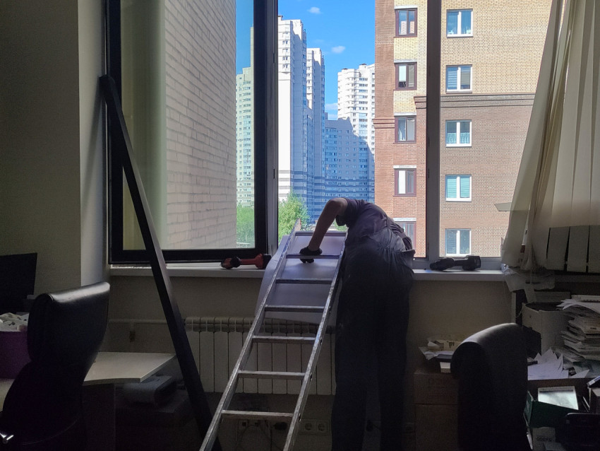 Мастер выполняет ремонт у подоконника, используя длинную алюминиевую лестницу