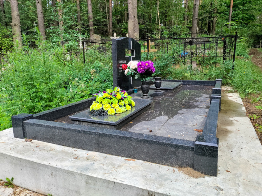 Полированный гранитный комплекс захоронения с цветами и вазами в лесу