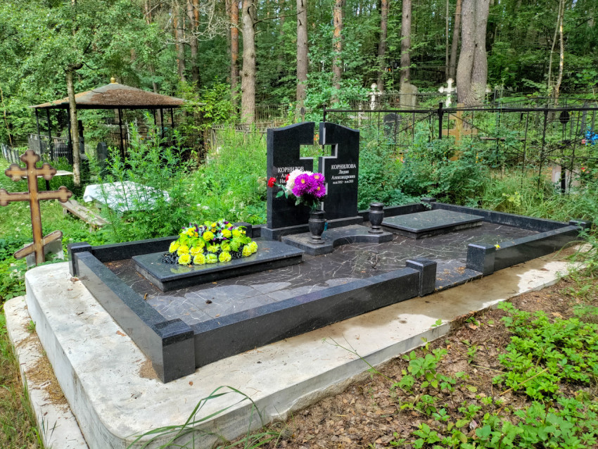 Семейное захоронение из чёрного гранита на фоне деревьев и кладбищенных оград