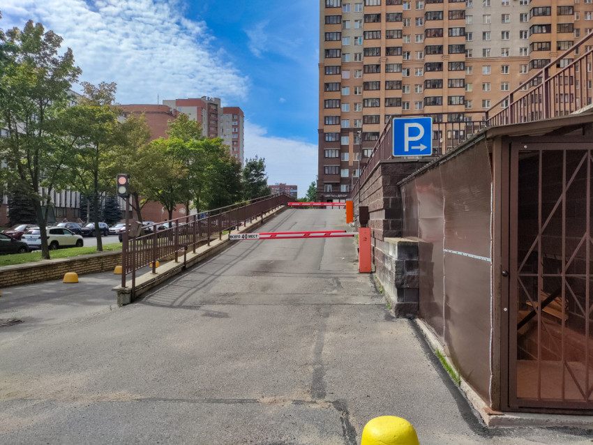 Подъём к парковке с шлагбаумом и пешеходным ограждением вдоль проезда