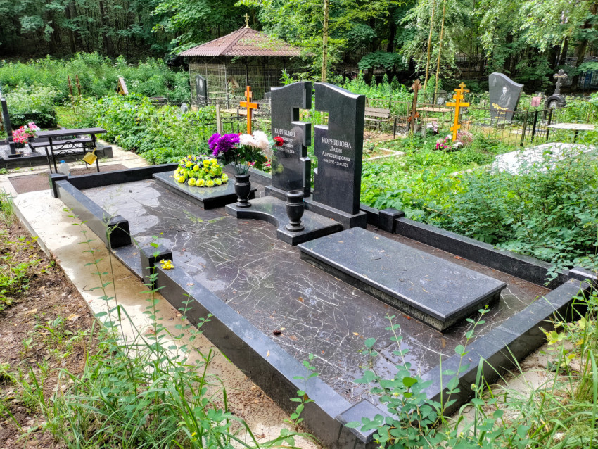 Панорама кладбищенного участка с гранитной плитой, крестами и зелёной растительностью