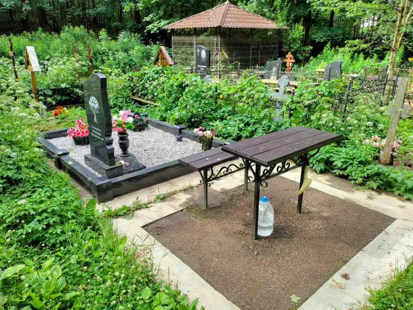 Лесное кладбище с могилами, цветами и столом для поминовения на площадке
