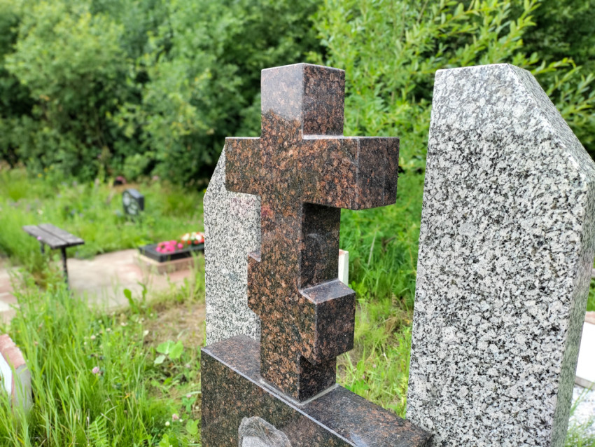 Крупный план гранитных надгробий с крестом на фоне зелени кладбища