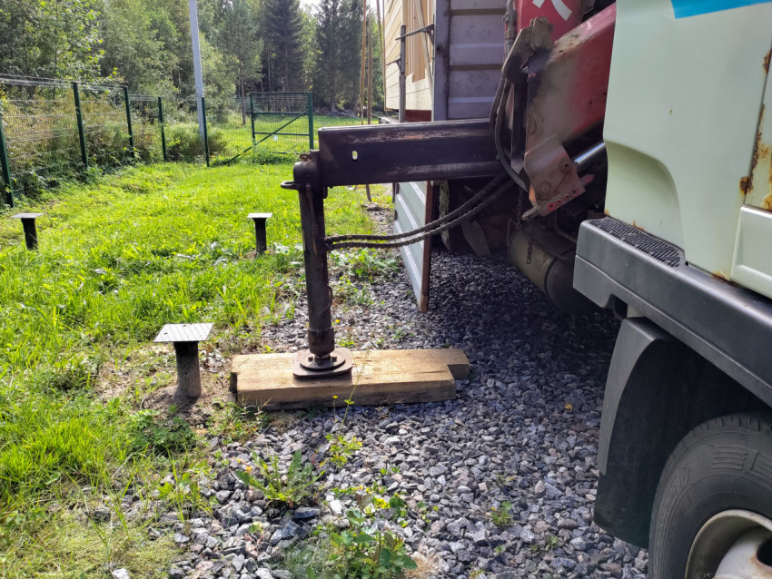 Выдвижная опора крана-манипулятора на деревянных подкладках рядом с винтовыми сваями на участке